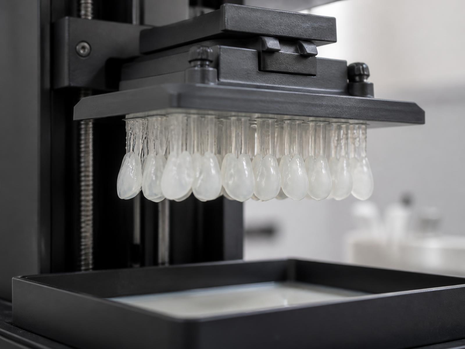 Resin 3D printer lifting a platform of ceramic-white veneer shells in a dental laboratory